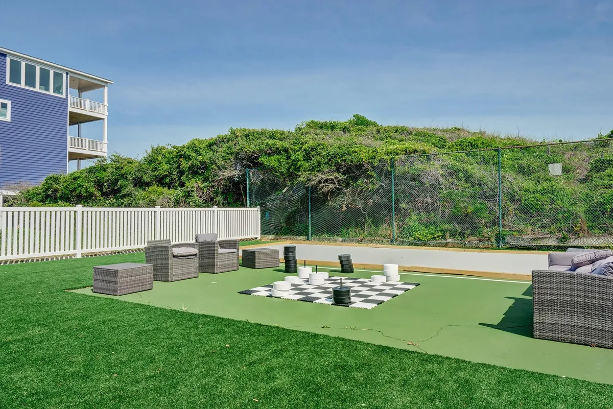 A spacious outdoor area featuring a large, oversized checkers game set on a green lawn, complemented by comfortable seating. The area is filled with sunlight and appears lively, perfect for group activities and socializing.