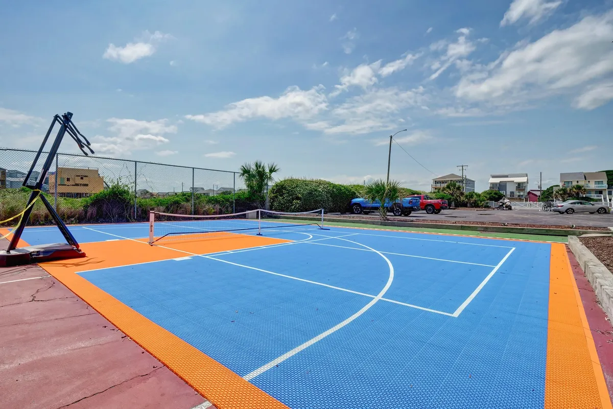 An outdoor sports court featuring both a basketball hoop and a tennis net over a colorful surface, inviting guests to play basketball, tennis, or simply hang out. The open-air setting suggests a vibrant, communal atmosphere perfect for energetic activities.