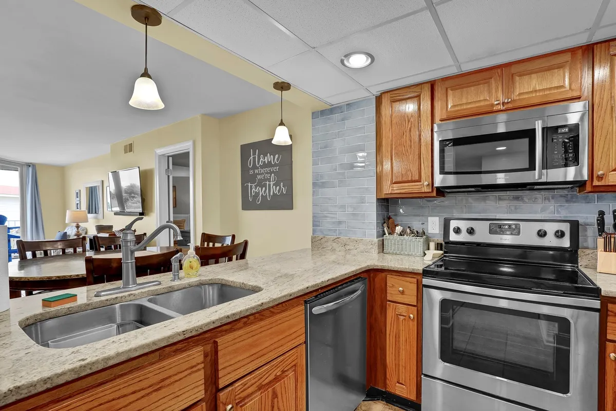 A modern kitchen with luxurious granite countertops, stainless steel appliances, elegant pendant lighting, and stylish decor. The setup is spacious and practical—perfect for preparing meals and entertaining family or friends.