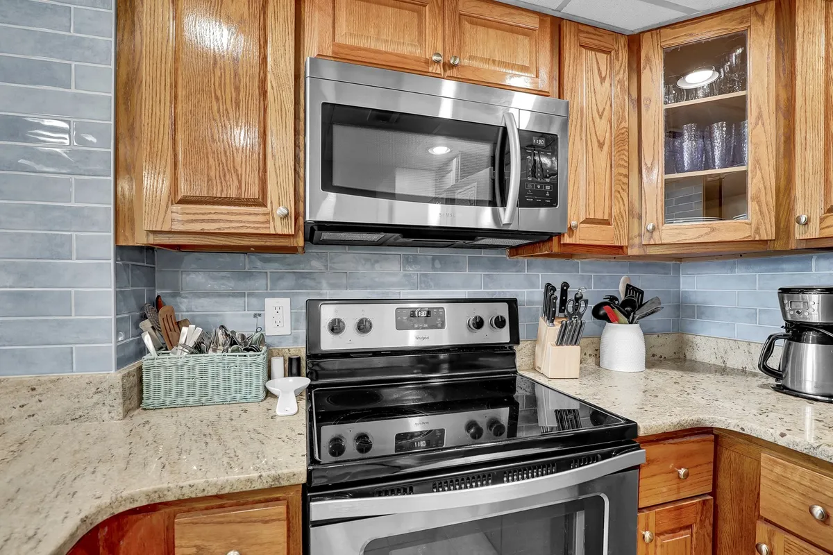 A well-appointed laundry area with a stainless steel microwave, black stove, granite countertop, and wooden cabinets. The design blends functionality and warmth, depicting the convenience of in-unit appliances.