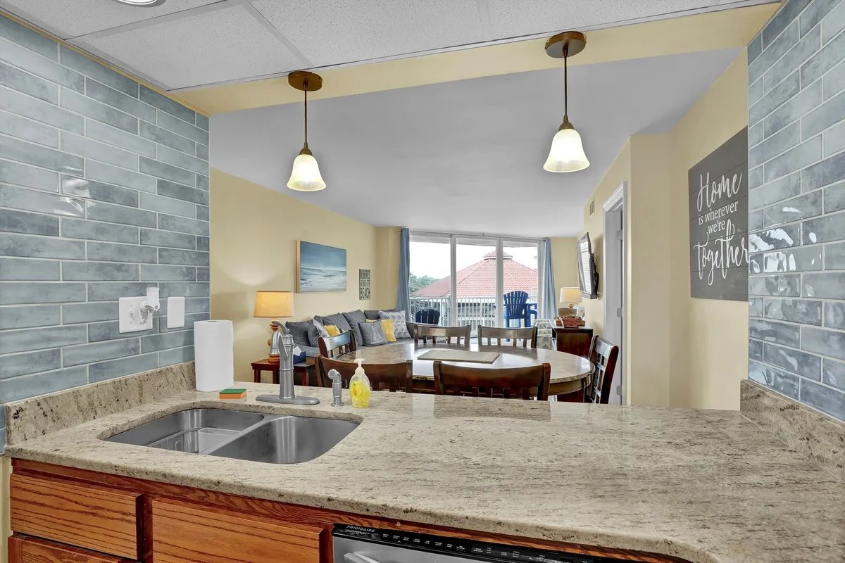 This image features a kitchen with a granite countertop, blue backsplash, dining table, and large windows. The bright, open space is designed for cooking, entertaining, and gathering, with enough room for families to create meals together or enjoy casual dining.
