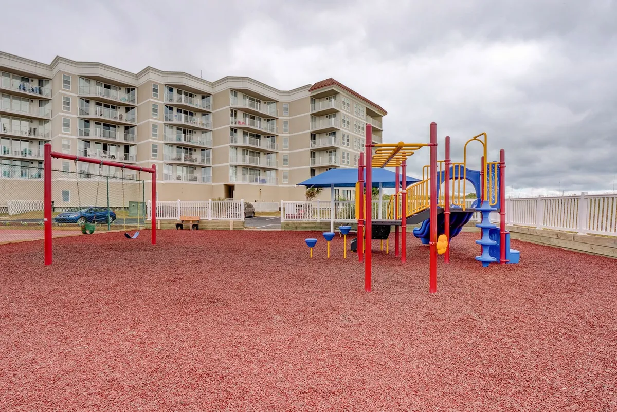 A colorful playground with swings and play structures sits in an open outdoor area, inviting children to play and families to gather. The vibrant equipment is designed for energetic outdoor recreation and joyful group activities.