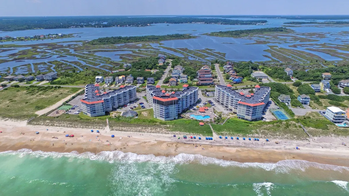 A lively scene showcases beachfront condos with a sparkling swimming pool, beach umbrellas, and the ocean just beyond. The area invites guests to swim, sunbathe, and participate in beach activities, perfectly blending poolside and seaside family fun.