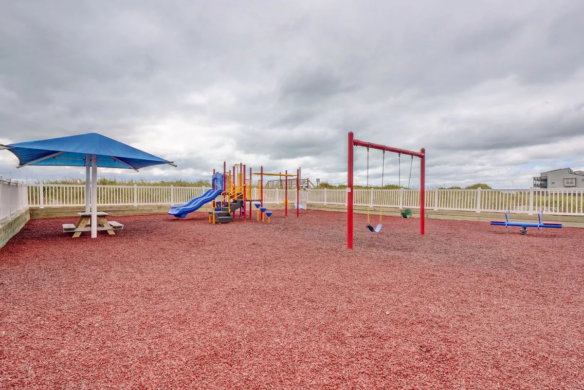 A colorful playground featuring various play structures, a swing set, and a shaded picnic area where children can play and families can relax together. The atmosphere is joyful and welcoming, ideal for younger guests.