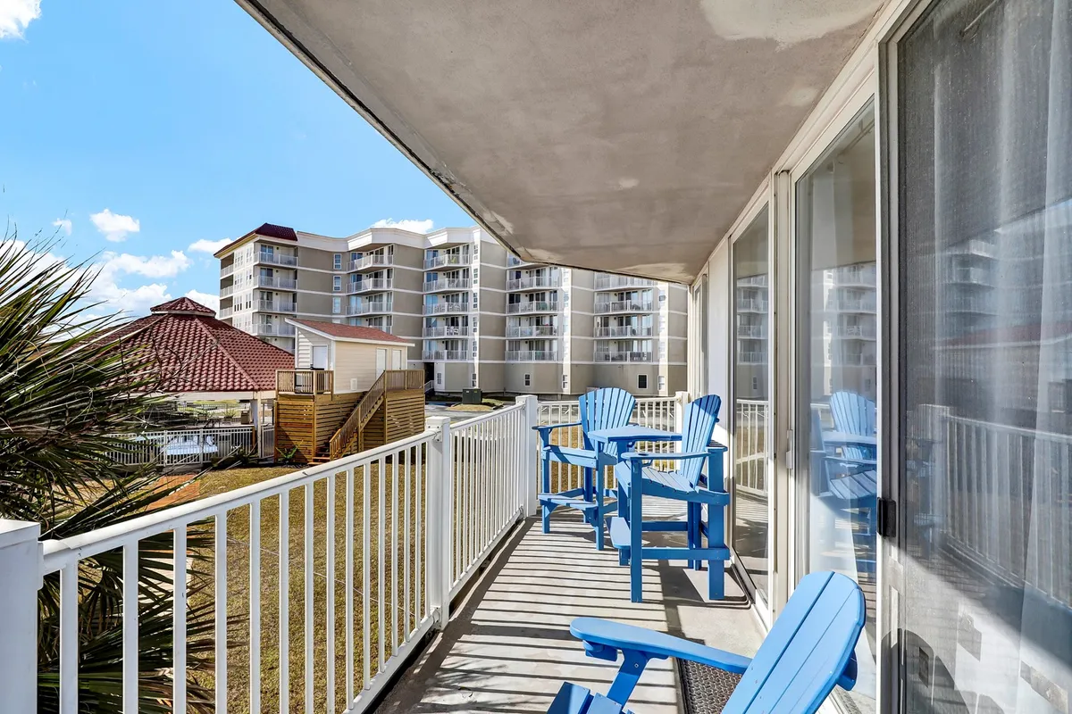 A cozy exterior seating area on a balcony with blue Adirondack chairs and a railing overlooking surrounding buildings. The space is ideal for morning coffee, evening relaxation, and intimate moments with loved ones, all while enjoying the fresh coastal air.