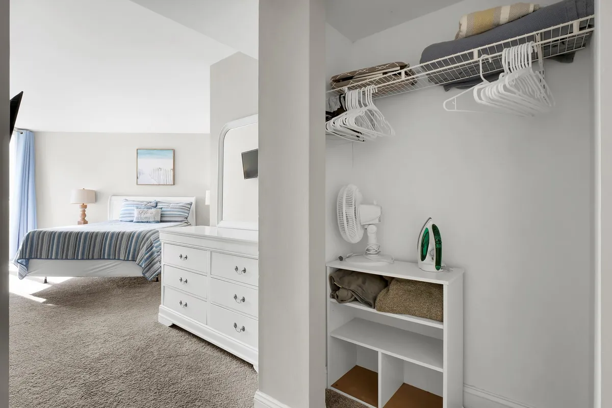 A cozy, tranquil bedroom scene with a bed featuring blue striped bedding, a white dresser, and a decorative painting on the wall. The space feels restful and private, perfect for unwinding after a day at the beach.